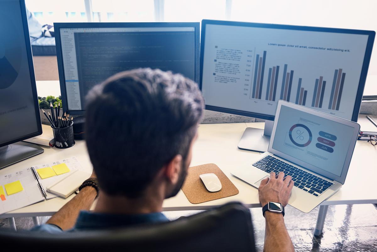 young professional works on data analysis on several computer monitors