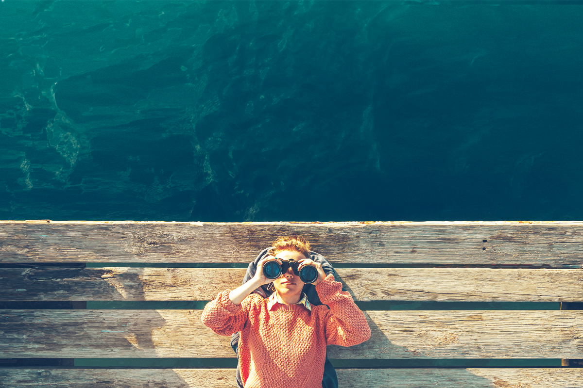 woman with binoculars sits on bench at ocean