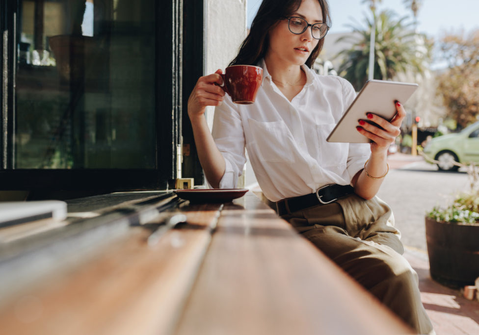 Female entrepreneur relaxing at coffee shop having coffee and reading email on her digital tablet. Businesswoman using digital tablet and drinking coffee at cafe.