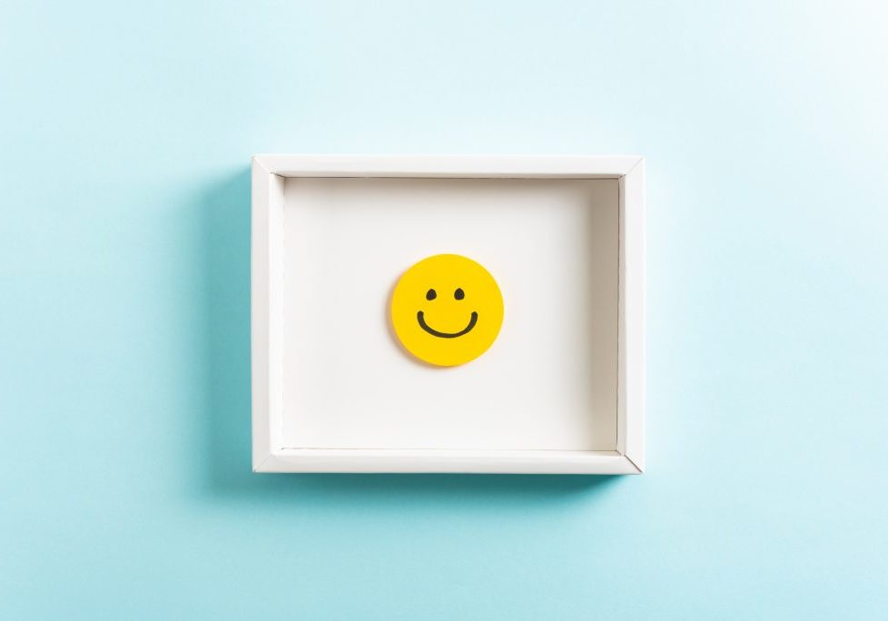 Happy diploma concept. Concept of well-being, well done, feedback, employee recognition award. Happy yellow smiling emoticon face frame hanging on blue background.